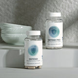 Two bottles of dietary supplement capsules promoting bone, heart, and immune support, displayed on a minimalist white surface.