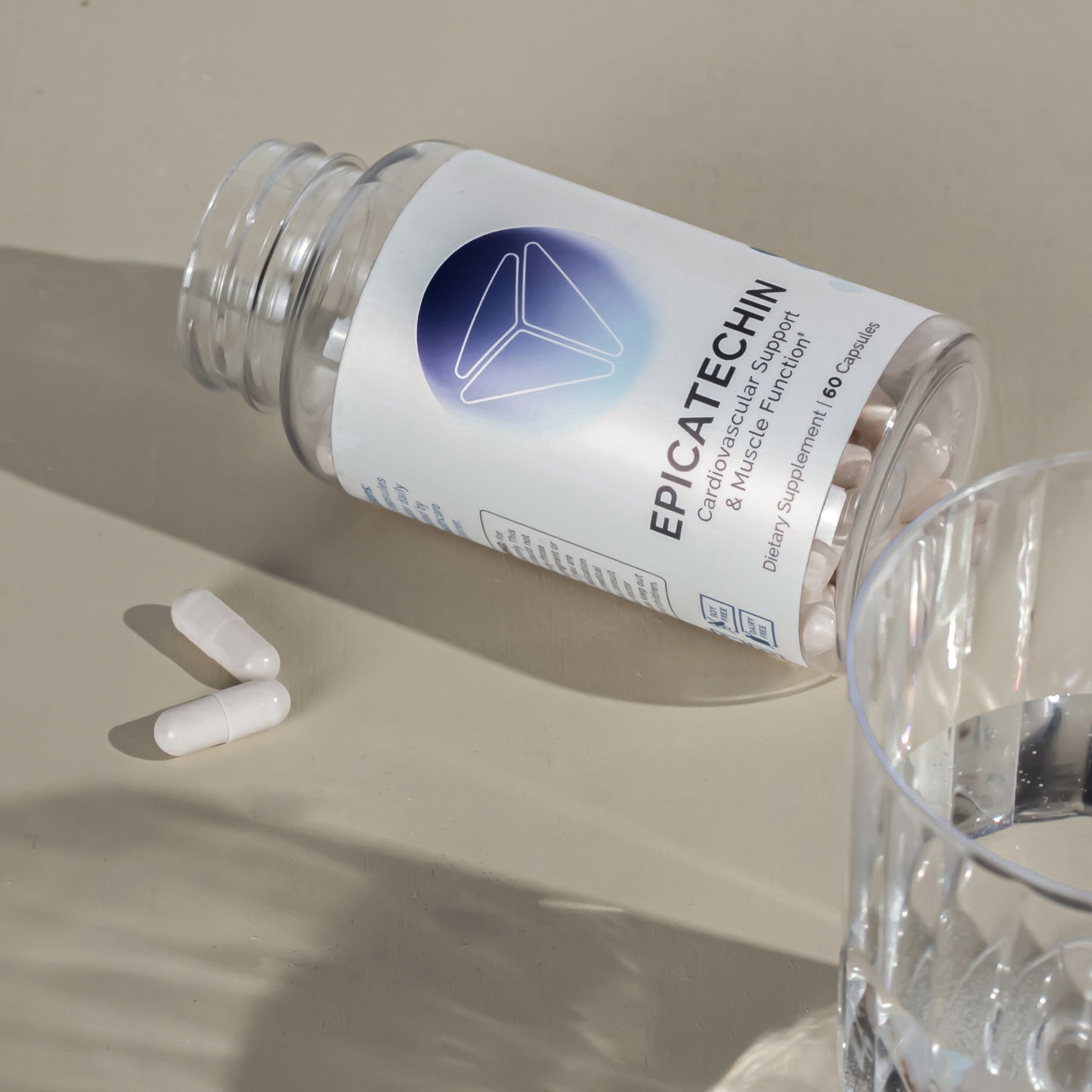White capsules spill from a clear bottle onto a beige surface, next to a glass of water.