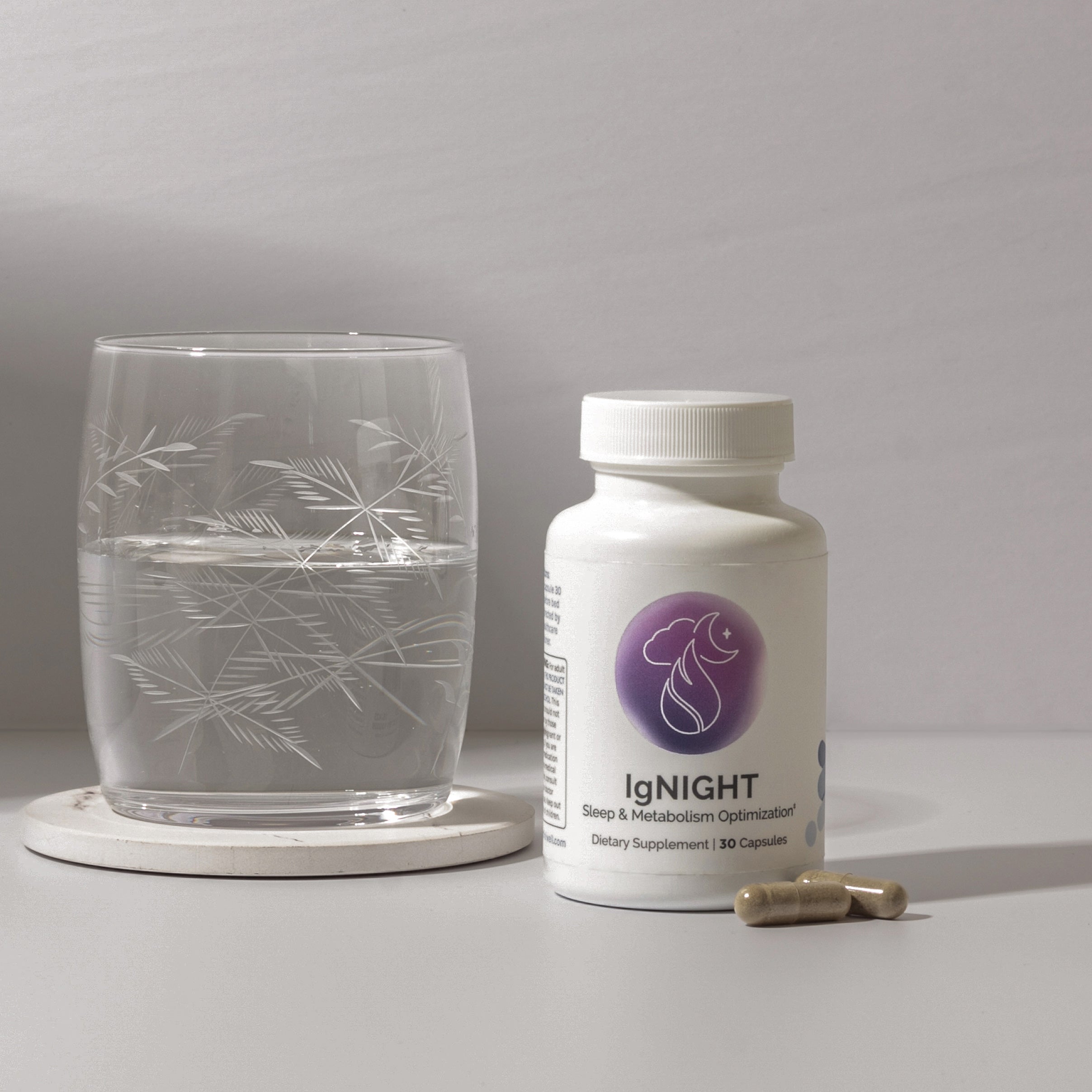 Sleep & metabolism supplement bottle with capsules, next to a glass of water.