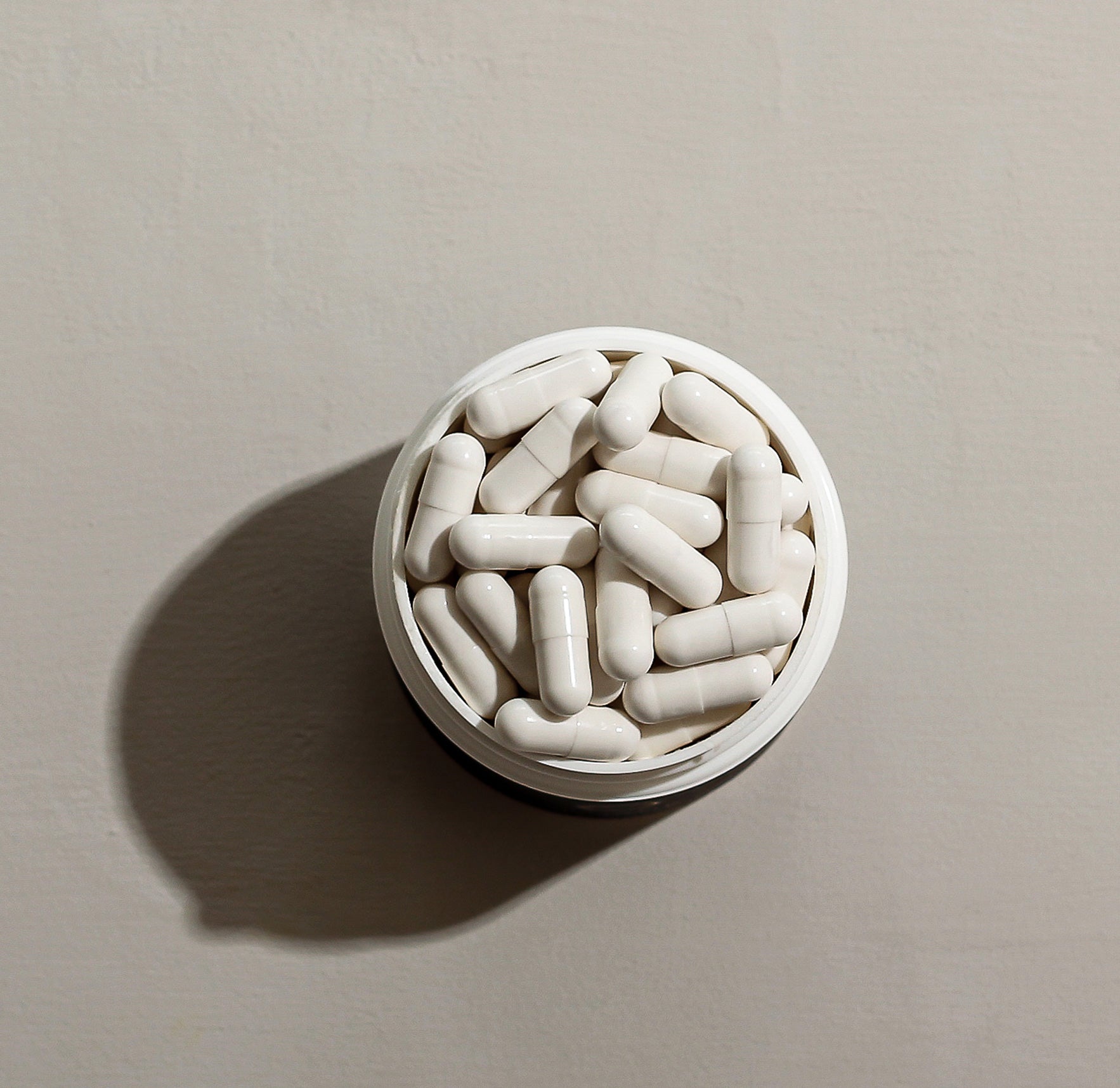 White capsules in a container, viewed from above on a neutral background.