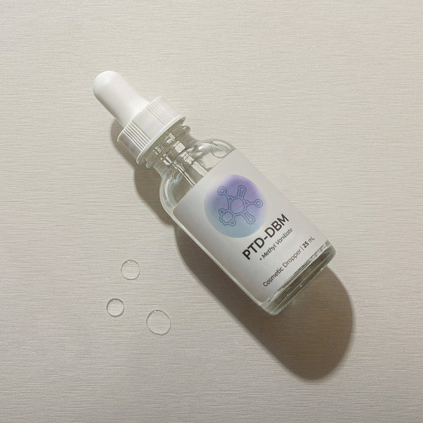 Infiniwell PTD-DBM cosmetic serum dropper bottle with visible serum droplets on light textured surface, 25 mL skincare serum