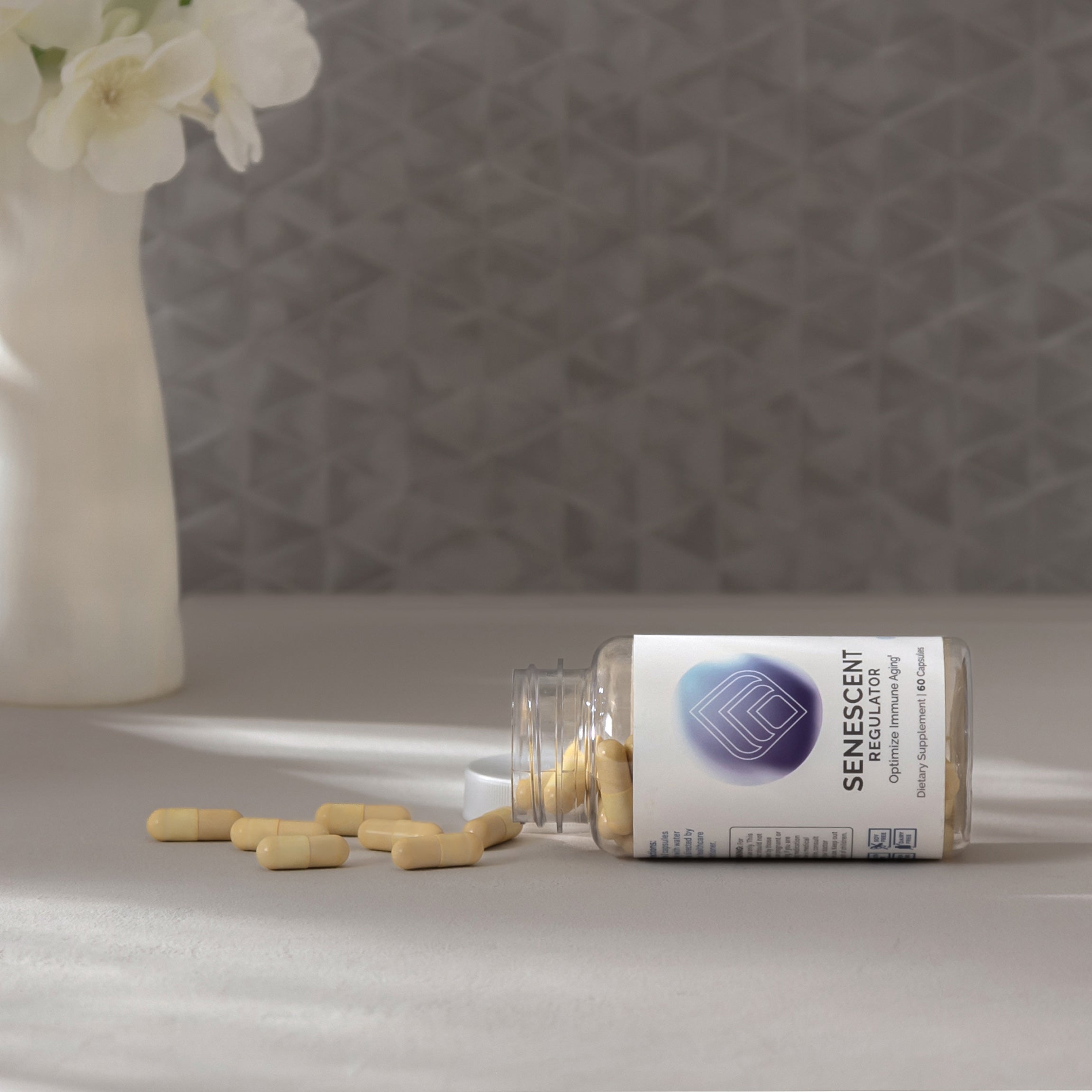 Beige capsules spill from a clear bottle onto a light gray surface, near white flowers.