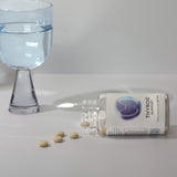 Beige tablets spilled from a clear supplement bottle, near a glass of water.