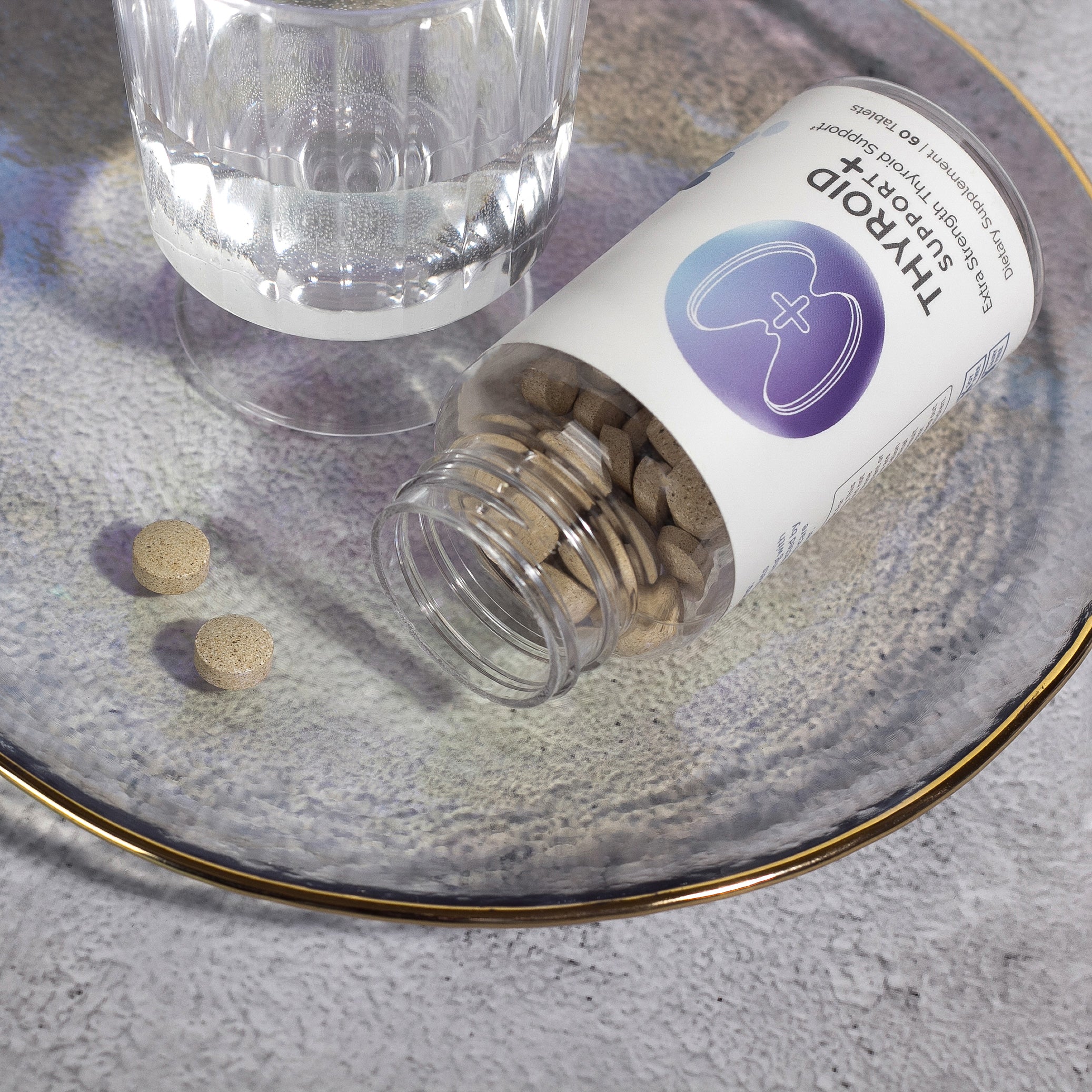 Thyroid support supplement pills spilled from bottle onto plate next to glass of water.