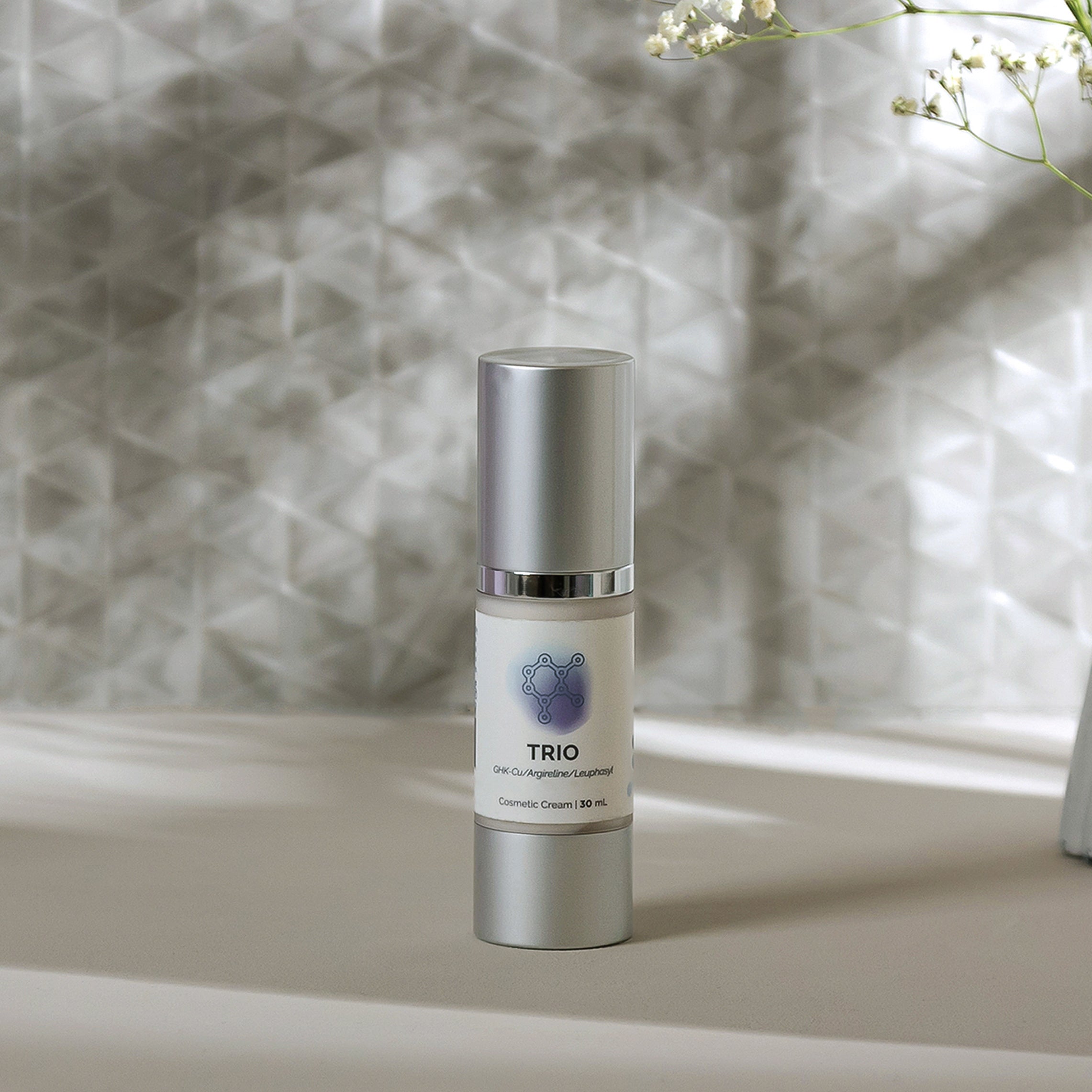 Silver bottle of cosmetic cream, 30ml, on a light beige surface with delicate flowers.