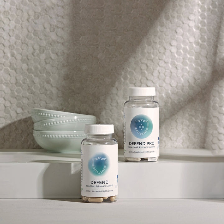Two dietary supplement bottles, showcasing bone, heart, and immune support benefits, displayed on a kitchen counter.
