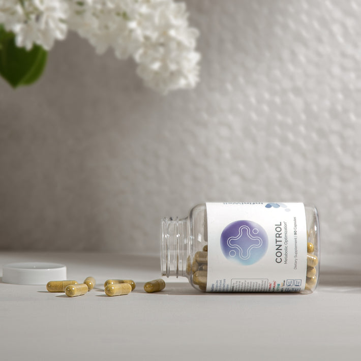 InfiniWell Control Metabolic Optimization supplement bottle with spilled capsules beside white flowers on a neutral surface.
