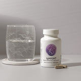 Sleep & metabolism supplement bottle with capsules, next to a glass of water.
