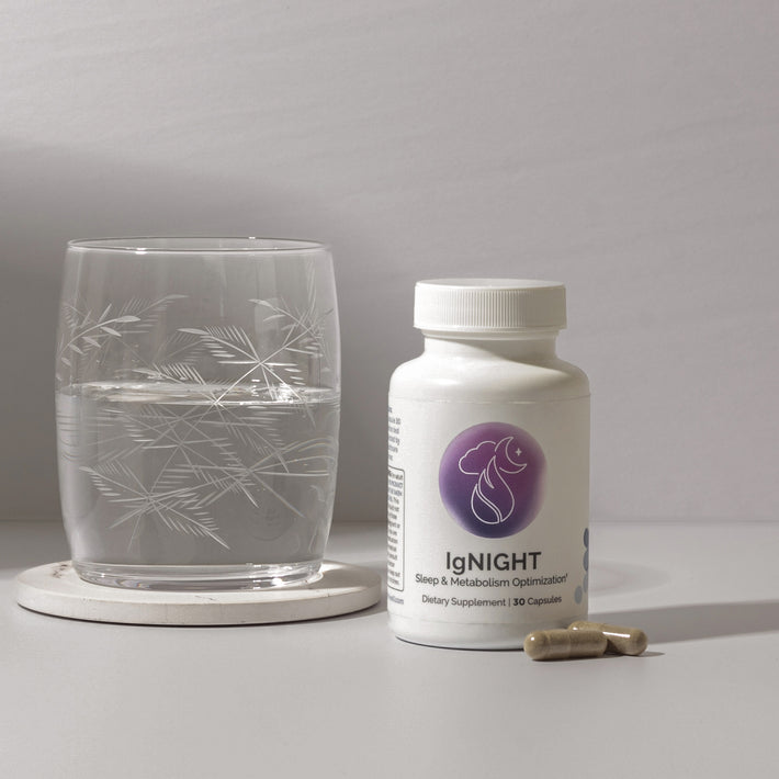 InfiniWell IgNIGHT sleep and metabolism support supplement bottle beside a glass of water and two capsules.