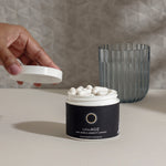 Open jar of InfiniAGE longevity supplement with white capsules beside a glass and hand lifting the lid.