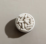 White capsules in a container, viewed from above on a neutral background.
