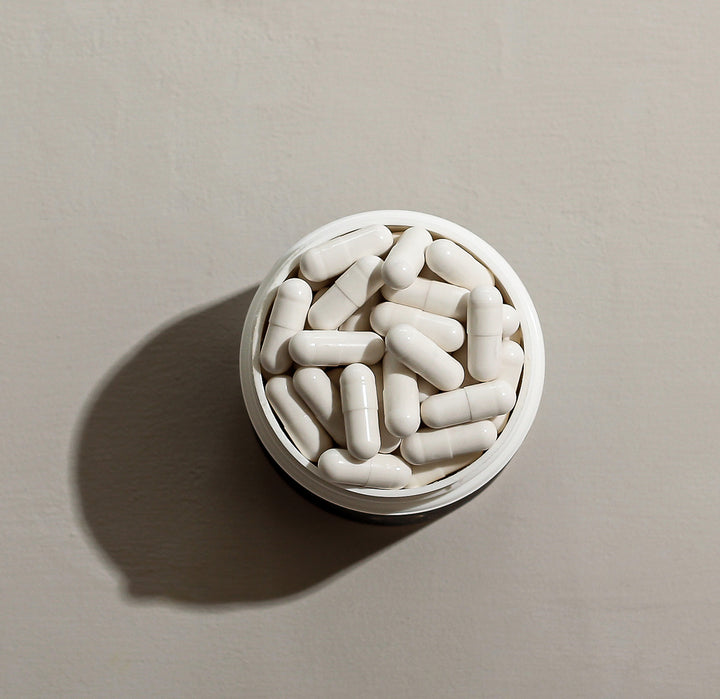 White capsules in a container, viewed from above on a neutral background.
