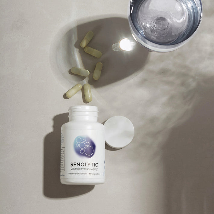 Infiniwell Senolytic optimize immune aging supplement bottle with loose capsules, open cap and glass of water above